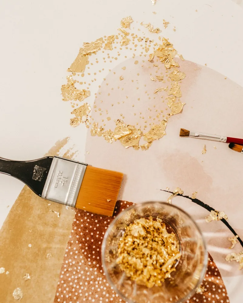 Fragmentos de pan de oro, brochas planas y un recipiente con recortes dorados sobre la mesa de trabajo